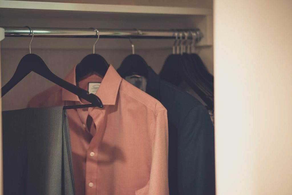 Stylish mens wardrobe featuring a formal suit and pink dress shirt neatly hung on hangers.