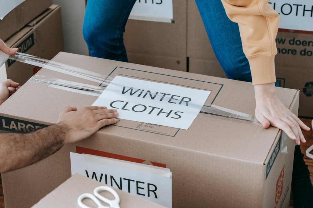 Close-up of hands packing a box labeled Winter Clothes for relocation, emphasizing organized moving.
